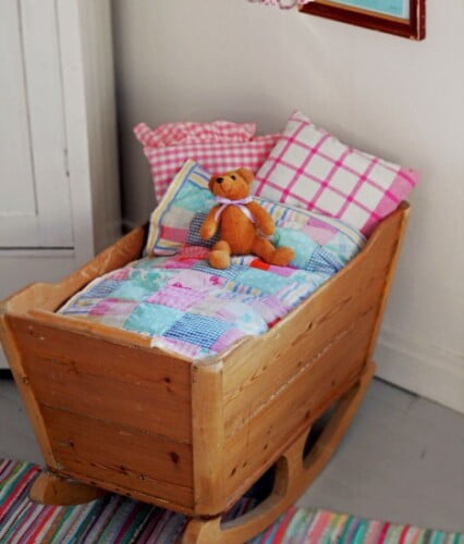 Barnvagga i naturfärgat trä bäddat med lapptäcke i rosa och blått.