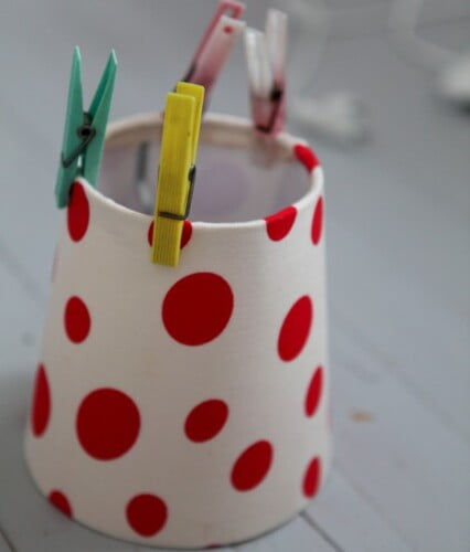 Rödprickig lampskärm med klädnypor i toppen.