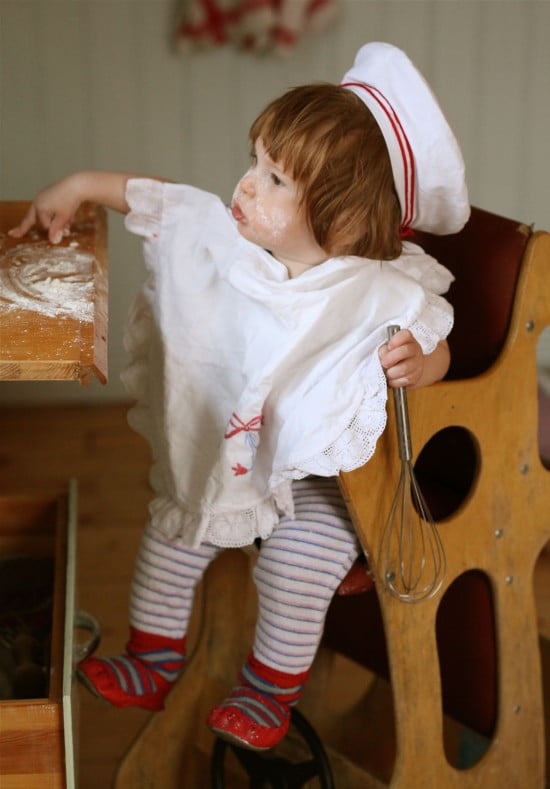 Liten bagare i barnstol och vita kläder så att inte mjölet syns - mer än på båda kinderna.