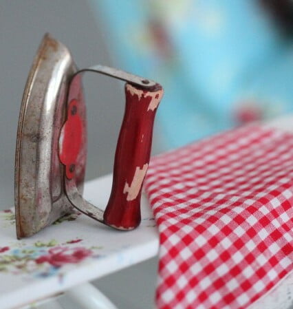 Leksaks strykjärn står på liten strykbräda med blommigt överdrag. Slitet och nött.