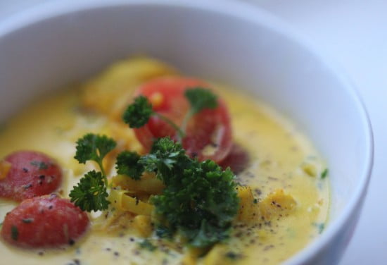 Vit skål med gul saffranssoppa/fisksoppa med körsbärstomat och persilja.