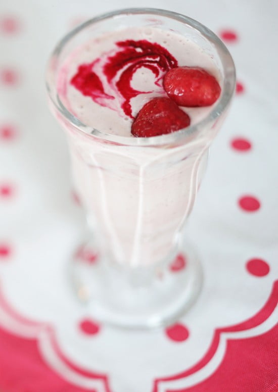 Ljus smoothie med jordgubbar på toppen i högt glas.