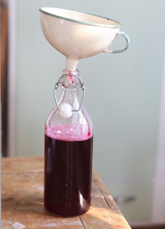 Glasflaska med tratt och röd vinbärssaft inuti.