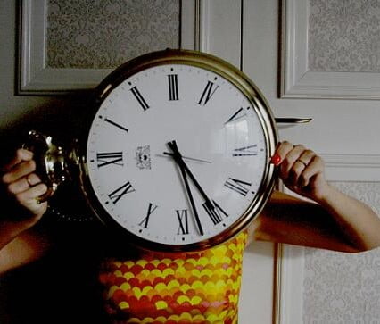 Stort urverk av gammal modell framför Clara i gul klänning.