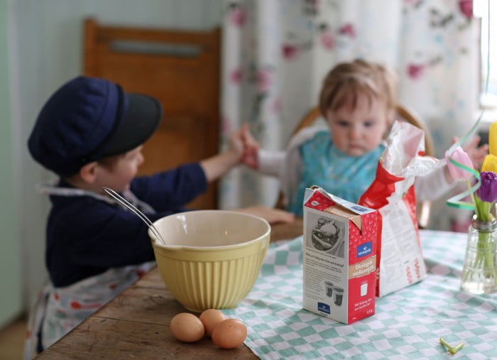 Småbröder med mjölk, mjöl och pannkaksmetens bunke på bordet.