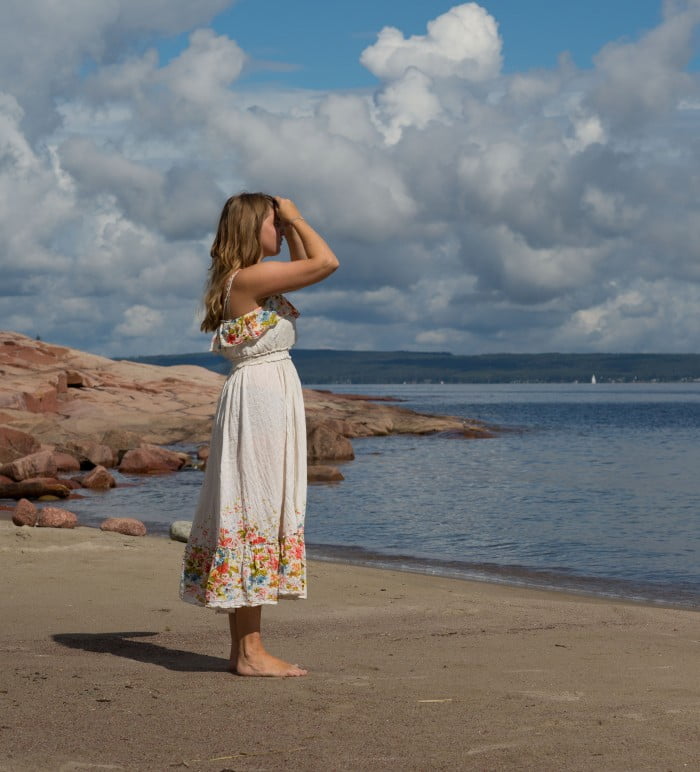 Clara står på sandstrand i sommarklänning.