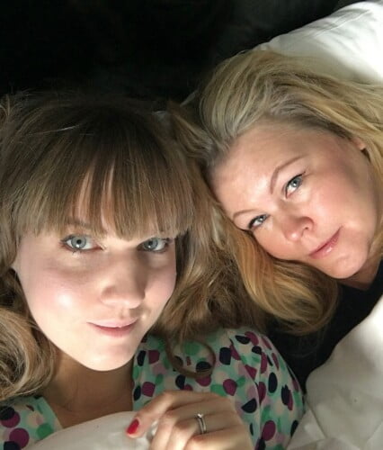 Clara och Erica nedbäddade i en hotellsäng med vita lakan.