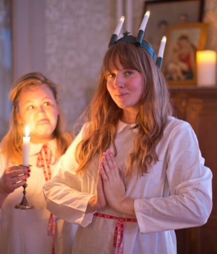 Clara och Erica klädda i lussekläder, Clara lucia och Erica tärna som räcker ut tungan mot Clara bakom hennes rygg. Ur En Underbar Pod.