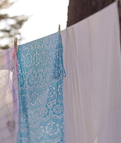 Ljusa tyger och kökshanddukar på klädlina utomhus.