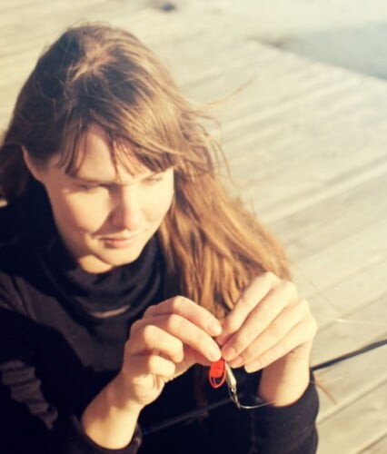 Clara fixar med fiskkrok på en brygga i solljus.