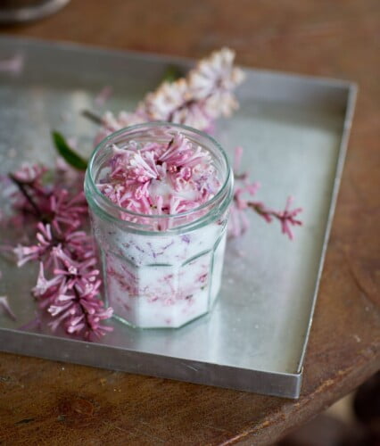 Liten glasburk fylld med socker, burken står på plåtbricka och runt omkring ligger syrenblommor.