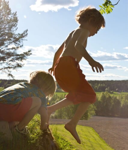 Pojkarna Bertil och Folke hoppar från en sten utomhus i sommarväder.