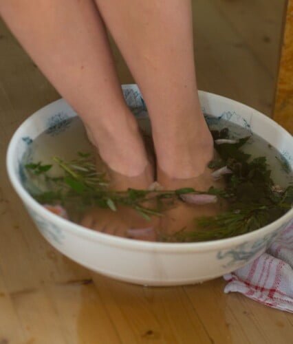 Nakna underben i stor porslinsskål fyllt med vatten, kryddor, blommor och tallris som flyter på ytan. Ur En underbar pod.