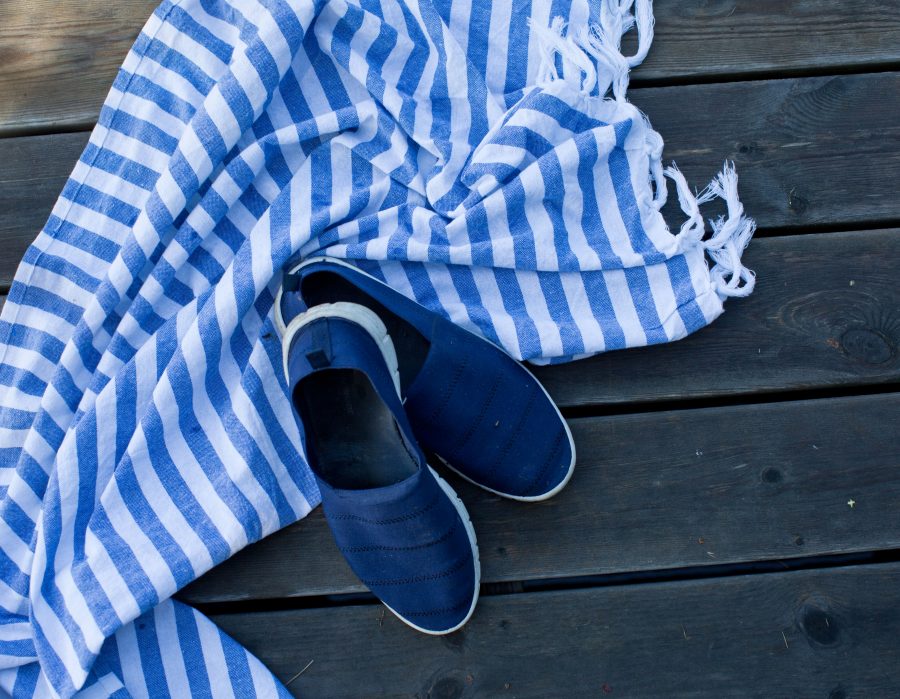 Blå sommarskor och en randig handuk på träbrygga.