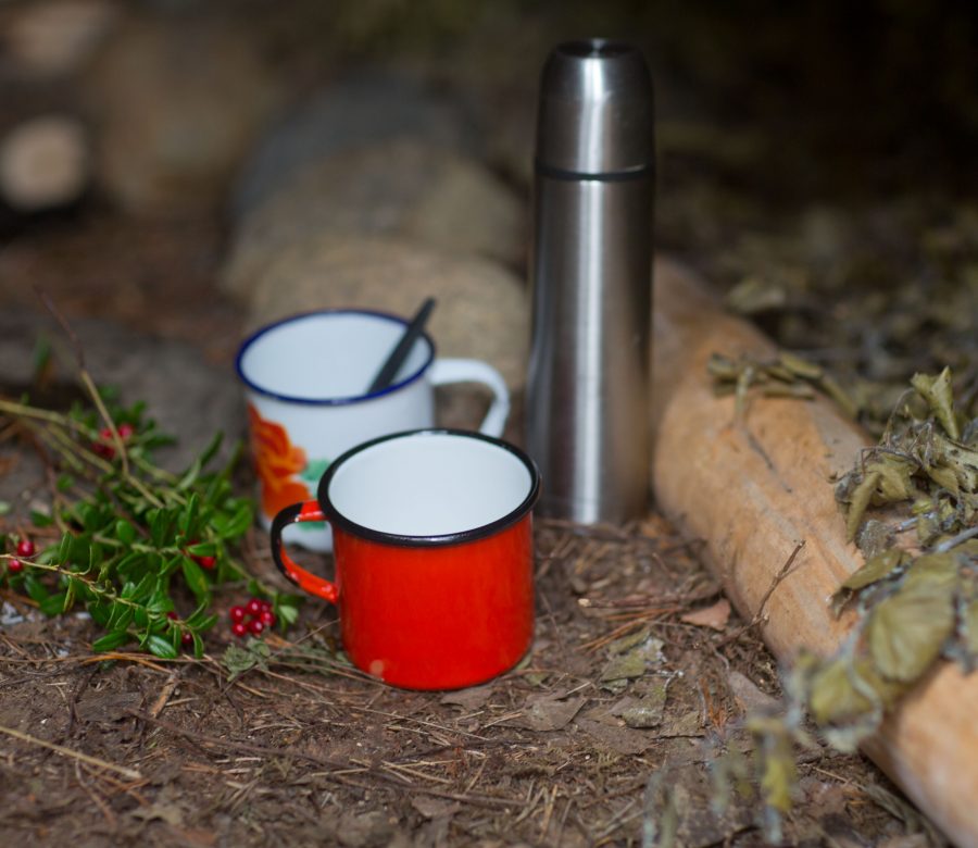 Färgglada emaljmuggar i rött och den ena med rosmönster, står intill silverfärgad metalltermos i kåta. Ur En Underbar Pod.