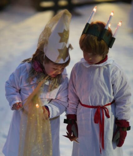 Barn i luciakläder utomhus på snöig väg.