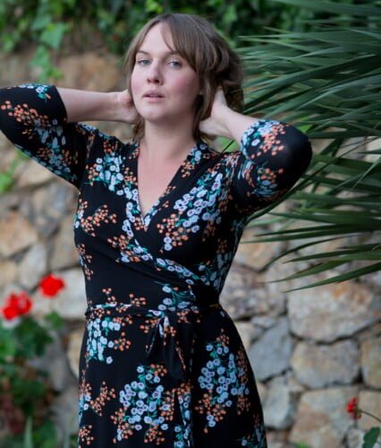 Clara i mörk miss clarity-klänning och armarna bakom huvudet tittar in i kameran.