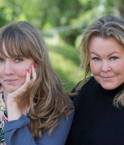 Clara och Erica tittar in i kameran, fotade utomhus med höstgrönska i bakgrunden. Ur En Underbar Pod.