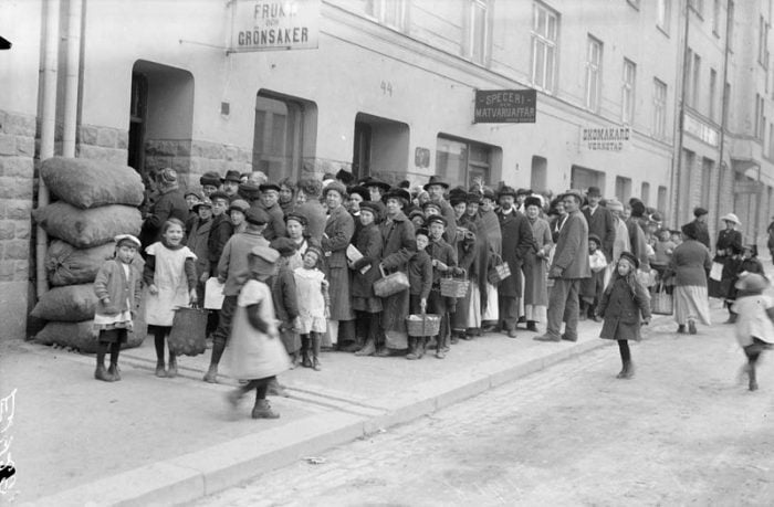 Svartvitt foto från 1917 där människor står i en lång bred potatiskö.