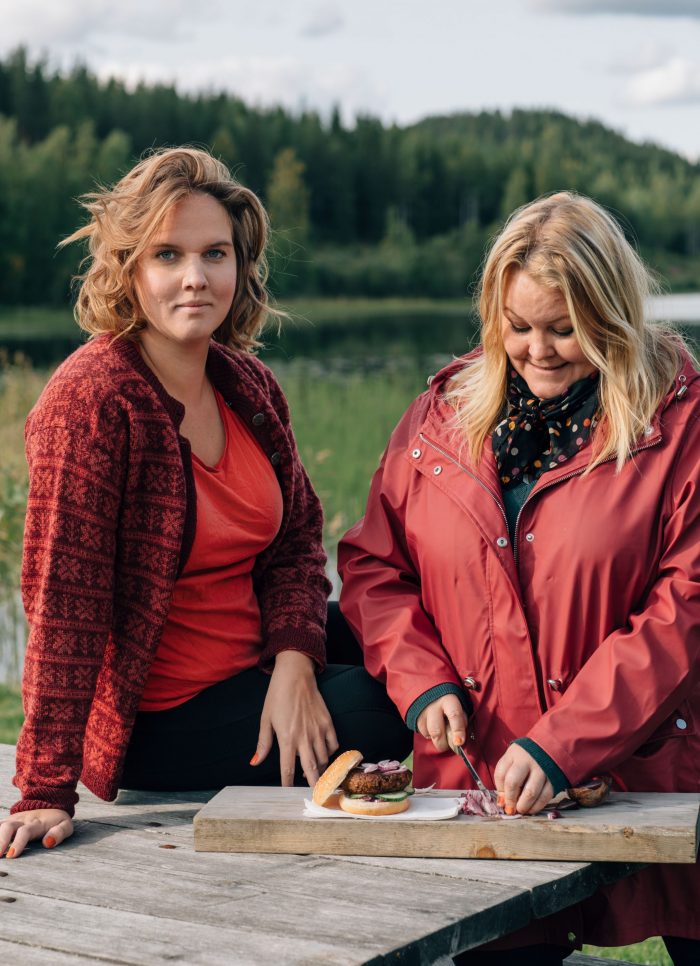 Clara och Erica ute i friska luften tidig höst, Erica har dukat upp vegburgare på skärbräda och skär lök.