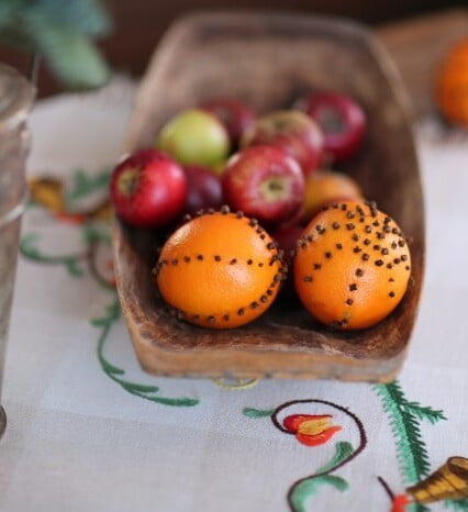 Gammeldags trätråg med juläpplen och apelsiner dekorerade med kryddnejlikor.