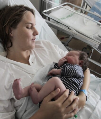 En nyförlöst Clara i sjuksäng som håller en av sina söner ömt i händerna.